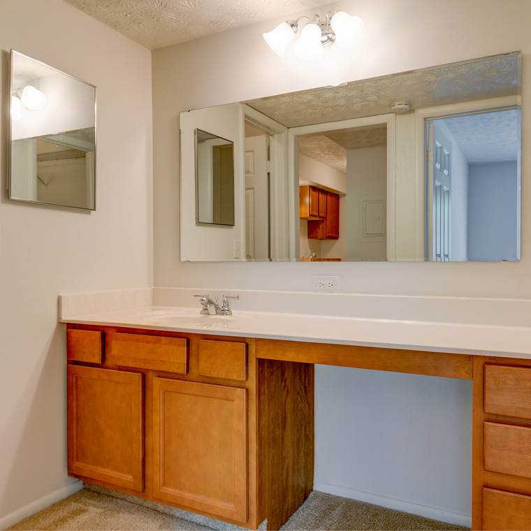 bathroom vanity with light wood and interior half wall separating toilet and tub